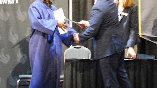 BHC president Dr. Jeremy Thomas handing certificate to GED grad Tony Johnson on stage