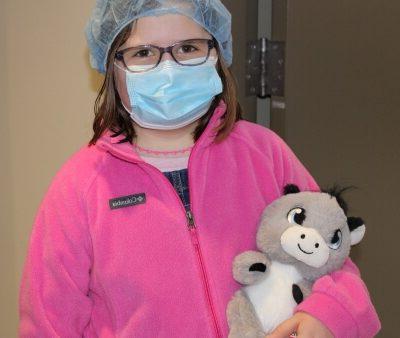 child wearing surgical mask and cap and holding stuffed animal